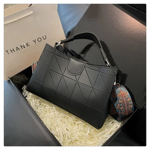 Detail of black geometric quilted handbag with ethnic patterned strap in a gift box