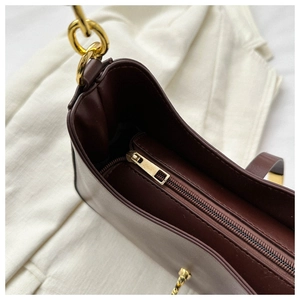 Détail de la fermeture éclair métallique et des anneaux dorés sur un sac bandoulière marron