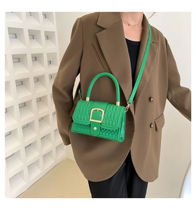 Dettaglio della borsa squadrata verde goffrata con fibbia dorata su modella