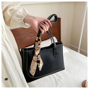 Detailed view of black leather tote bag with white contrast stitching and silk scarf
