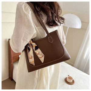 Detail of dark brown leather tote bag with white stitching and decorative silk scarf