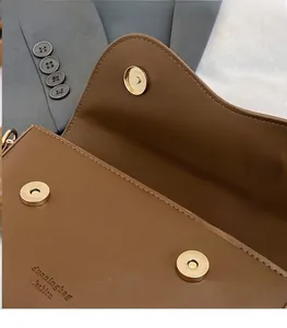 Detail shot of brown leather bag featuring golden magnetic snaps and brand logo
