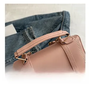 Detail of pink leather handbag featuring a cylindrical handle and gold metal hardware