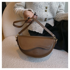 Close-up of brown saddle bag with gold metal buckles on a cozy cream textured sofa