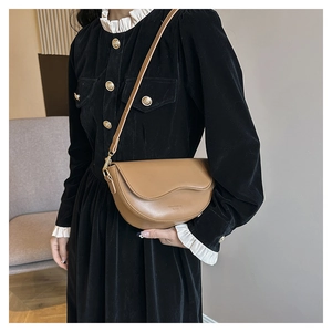 Detail of tan leather saddle bag with wave edge on a black velvet dress model