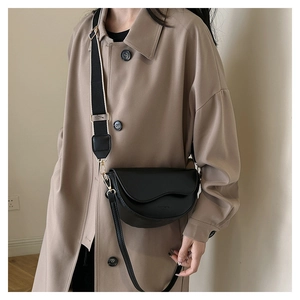 Detail of black semi-circle saddle bag with wide shoulder strap on khaki trench coat