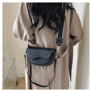 Detail of black saddle bag featuring wavy lid design and contrast wide fabric strap