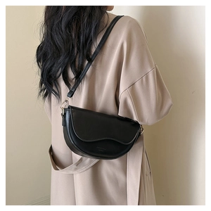 Close-up of black crescent saddle bag with gold hardware worn on a beige trench coat