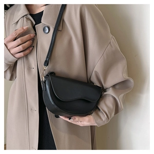 Detail of a black saddle bag with wavy flap design on a model wearing a camel coat
