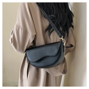 Detail of black saddle bag with fine leather texture and gold hardware on beige coat