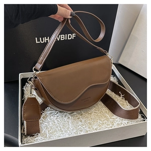Detail view of brown leather saddle bag with wide fabric strap in a premium gift box