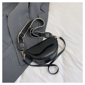 Detail of black leather saddle bag with wide canvas strap and gold hardware accents