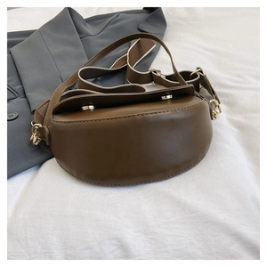 Detail of a brown leather saddle bag featuring a wide striped strap and golden hardware