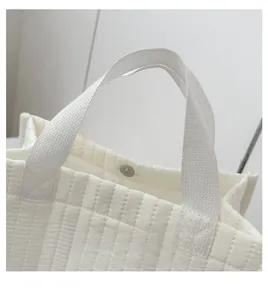 Detailed view of white quilted tote bag with vertical stripes and sturdy fabric handles