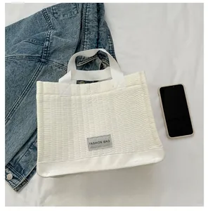 Detail of white quilted tote bag with FASHION BAG label showing size relative to a phone