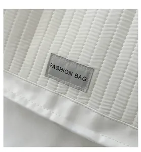 Close-up of white vertical quilted linen bag featuring a modern Fashion Bag woven label