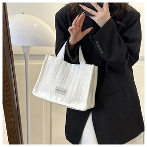 Detail of white quilted tote bag featuring vertical stitching and a fashion bag label