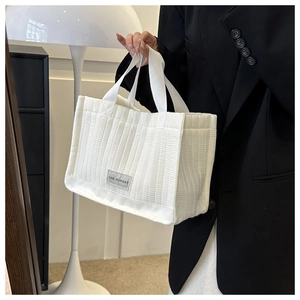 Close-up of a white tote bag featuring vertical quilted texture and fashion woven label