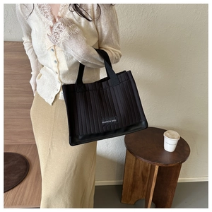 Detail of vertical quilted black tote bag with fashion label and reinforced glossy base