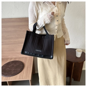 Detailed shot of black quilted tote bag with vertical stitching and fashion label