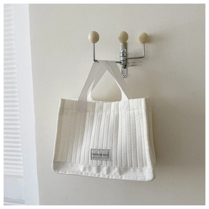 Detail of white quilted fabric tote bag with Fashion Bag tag on a minimalist wall hook