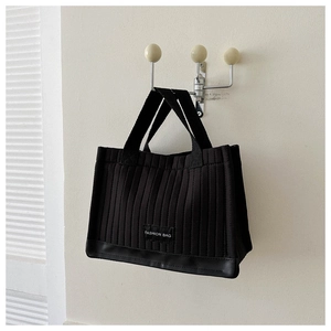Detail of black quilted tote bag with vertical stitching hanging on a wall hook