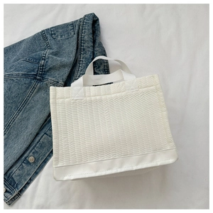 Detail of white quilted tote bag with vertical stripes and reinforced leather bottom