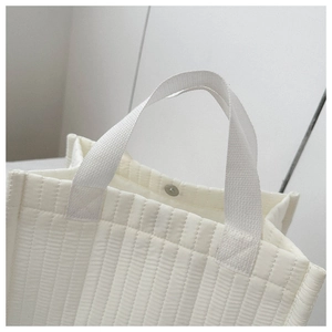 Detail of white quilted tote bag featuring fabric handles and secure silver metal snap button