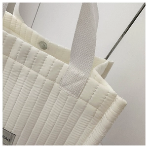Detail view of vertical quilted white tote bag featuring a silver magnetic clasp closure