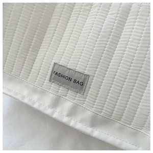 Detail of white quilted fabric with vertical stitching and Fashion Bag label on a tote