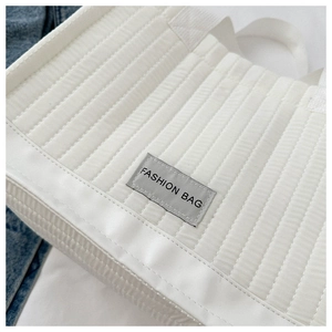 Detail of white quilted tote bag with vertical stitching and Fashion Bag label