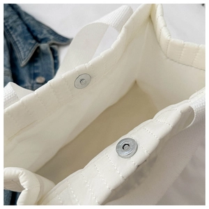Detail of white quilted tote bag featuring silver magnetic closure and woven straps