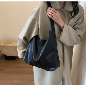 Detail of minimalist black PU leather tote bag worn with a beige trench coat