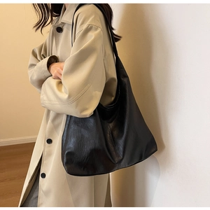 Detail of a black oversized faux leather hobo shoulder bag styled with a khaki trench coat