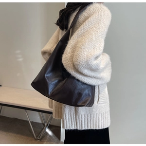 Detail of a large coffee brown faux leather tote bag worn by a model in casual attire
