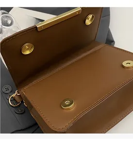 Detail of brown leather bag showing gold magnetic closures and precision stitching