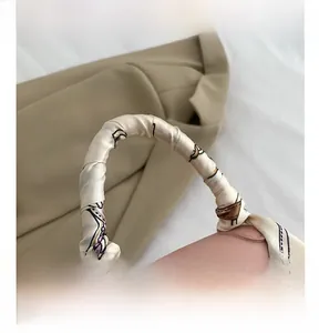 Detail of light pink leather handbag handle wrapped in printed silk scarf with elegant bow