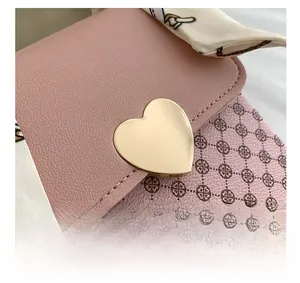 Close-up of pink leather crossbody bag with heart buckle and decorative silk scarf