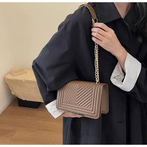Detail of V-quilted brown leather crossbody bag with elegant gold metal chain strap