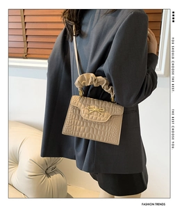 Detailed view of beige embossed crossbody bag with butterfly clasp and pleated handle