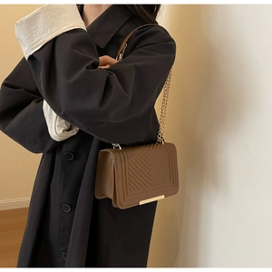 Detail of brown quilted shoulder bag with gold chain strap worn with a black coat