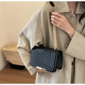 Detail of black V-quilted flap bag with gold chain strap and metallic lock closure