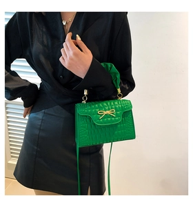 Detail of bright green faux crocodile handbag featuring a gold bow and ruffled handle
