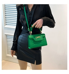 Close-up of vibrant green crocodile pattern handbag with gold bow detail on a model