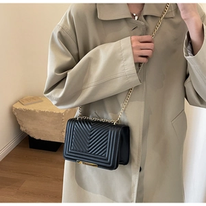 Detailed view of black quilted crossbody bag with gold chain strap worn by a model