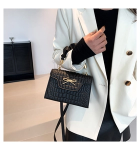 Detail of black crocodile texture handbag with golden bow buckle on white blazer outfit