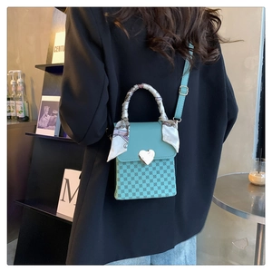 Detail of mint green crossbody bag with heart clasp and ribbon handle on a model