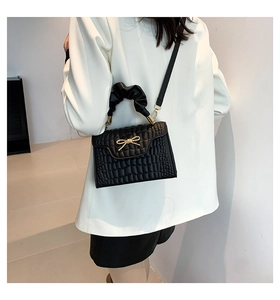 Detail of crossbody bag featuring black crocodile pattern and gold bow charm on model