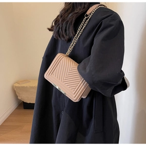 Detail of nude chain shoulder bag with V-quilted texture and gold metal trim on black coat
