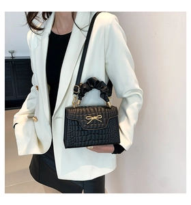 Detail of black crocodile embossed handbag with gold bow clasp and ruched handle